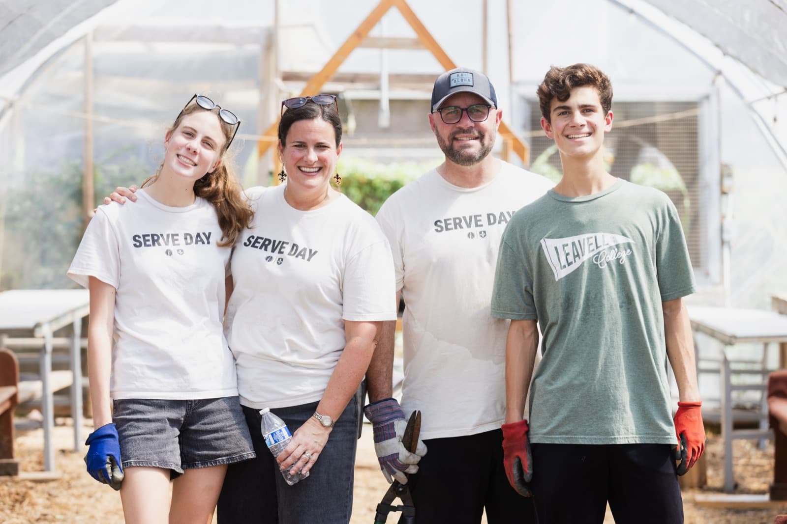 Four Serve Day volunteers smiling inside a community garden greenhouse